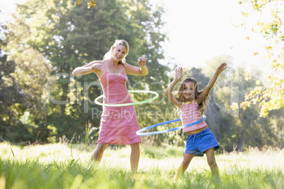 Woman and young girl outdoors using hula hoops and smiling