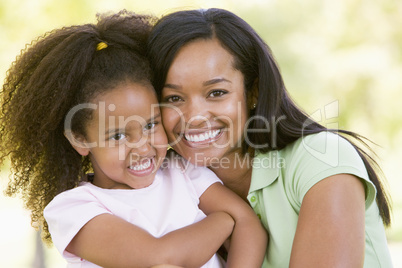 Woman and young girl outdoors embracing and smiling