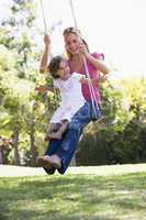 Woman and young girl outdoors on tree swing smiling