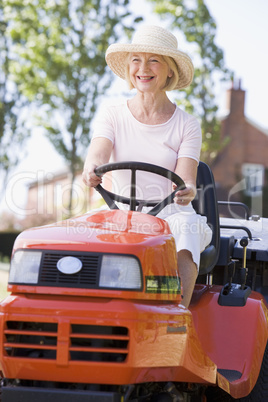 Woman outdoors driving lawnmower smiling