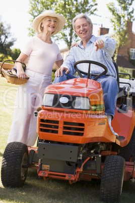 Couple outdoors with tools and lawnmower pointing and smiling