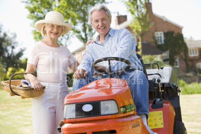 Couple outdoors with tools and lawnmower smiling