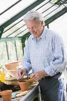 Man in greenhouse putting seed in pot smiling