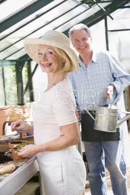 Woman in greenhouse planting seeds and man holding watering can