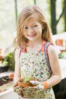 Young girl in greenhouse holding potted plant smiling