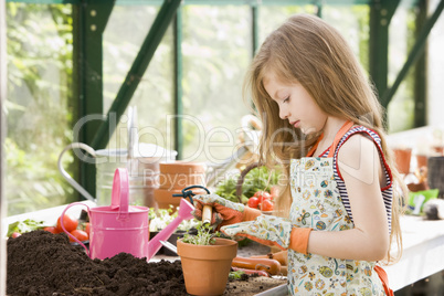 Young girl in greenhouse putting plant in pot