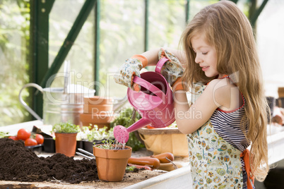 Young girl in greenhouse watering potted plant smiling
