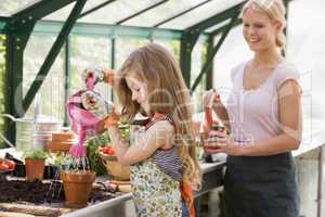Young girl in greenhouse watering plant with woman holding pot s