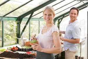 Couple in greenhouse raking soil in pots smiling