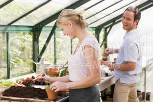 Couple in greenhouse putting soil in pots smiling