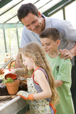 Man in greenhouse helping two young children putting soil in pot