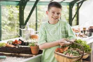 Young boy in greenhouse holding basket of vegetables smiling