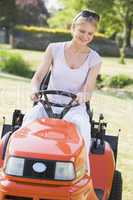 Woman outdoors driving lawnmower smiling