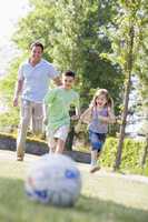 Man and two young children outdoors playing soccer and having fu