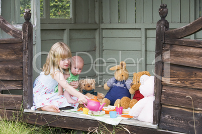 Young girl in shed with baby playing tea