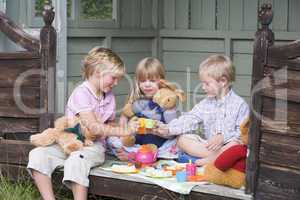 Three young children in shed playing tea and smiling