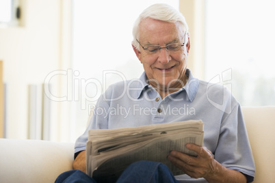 Man in living room reading newspaper smiling