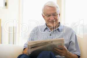 Man in living room reading newspaper smiling