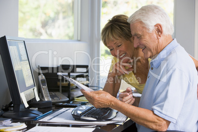 Couple in home office with computer and paperwork smiling