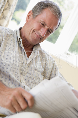 Man in living room reading newspaper smiling