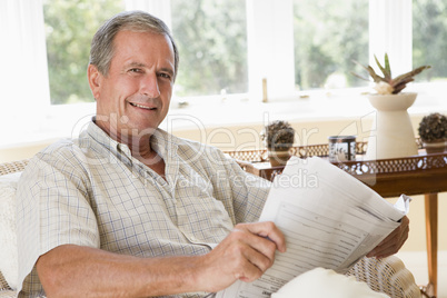 Man in living room reading newspaper smiling