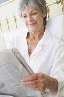 Woman in bedroom with newspaper smiling