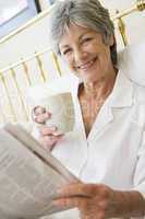 Woman in bedroom with coffee and newspaper smiling