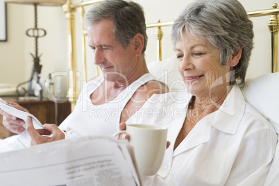 Couple in bedroom with coffee and newspapers smiling