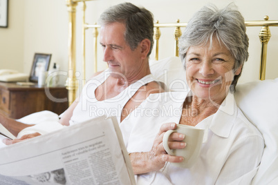 Couple in bedroom with coffee and newspapers smiling