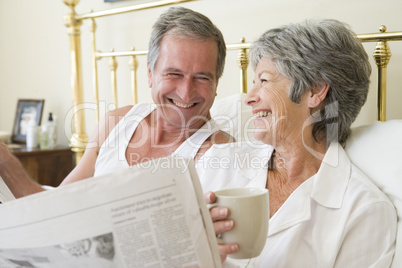 Couple in bedroom with coffee and newspapers smiling