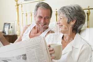 Couple in bedroom with coffee and newspapers smiling
