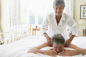 Woman giving man massage in bedroom smiling