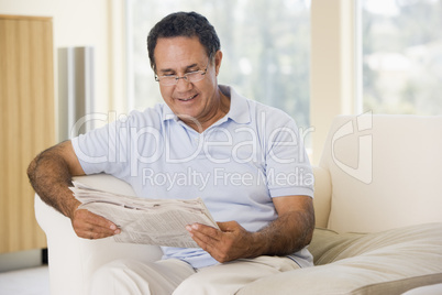 Man in living room reading newspaper smiling