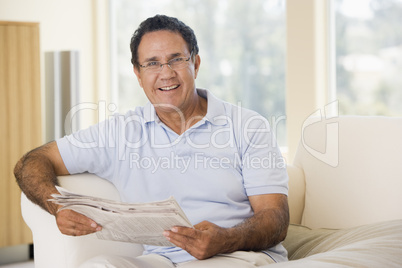 Man in living room reading newspaper smiling