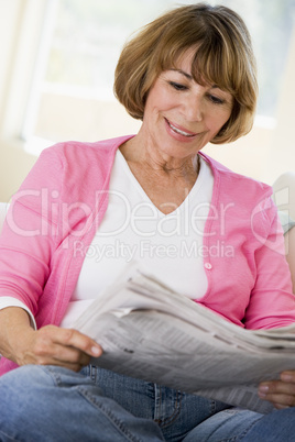 Woman in living room reading newspaper smiling