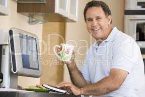 Man in kitchen with computer and coffee smiling