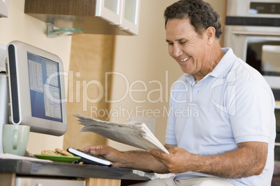 Man in kitchen with computer and newspaper smiling