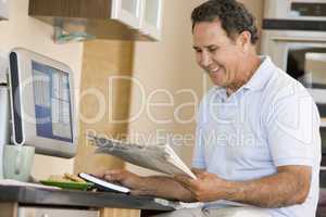 Man in kitchen with computer and newspaper smiling