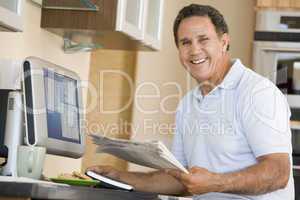 Man in kitchen with computer and newspaper smiling