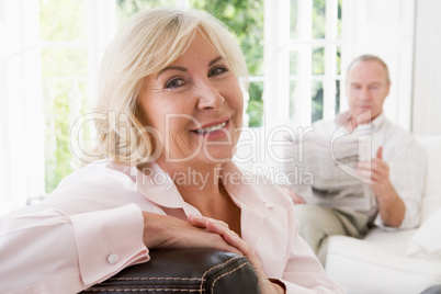 Woman in living room smiling with man in background reading news