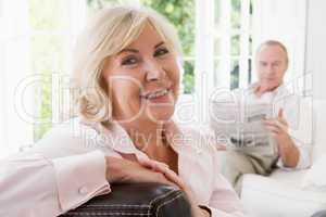 Woman in living room smiling with man in background reading news