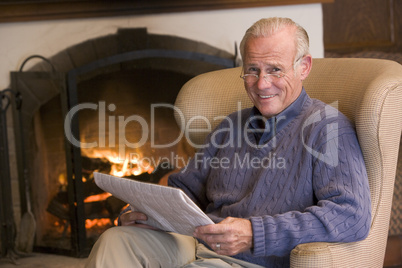 Man sitting in living room by fireplace with newspaper smiling