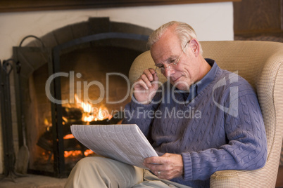 Man sitting in living room by fireplace with newspaper