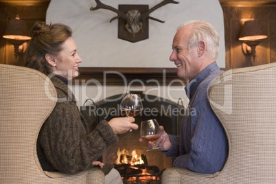 Couple sitting in living room by fireplace with drinks smiling