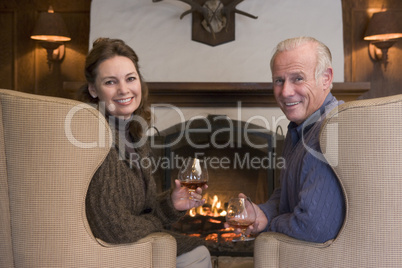 Couple sitting in living room by fireplace with drinks smiling