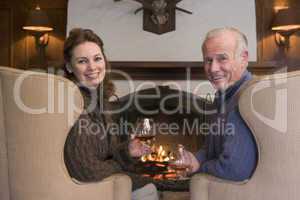 Couple sitting in living room by fireplace with drinks smiling