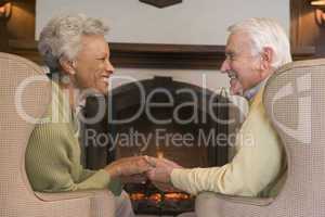 Couple sitting in living room by fireplace holding hands and smi