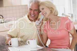 Couple in kitchen with coffee using telephone together and smili