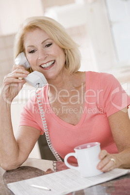 Woman in kitchen with coffee using telephone smiling