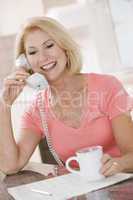 Woman in kitchen with coffee using telephone smiling